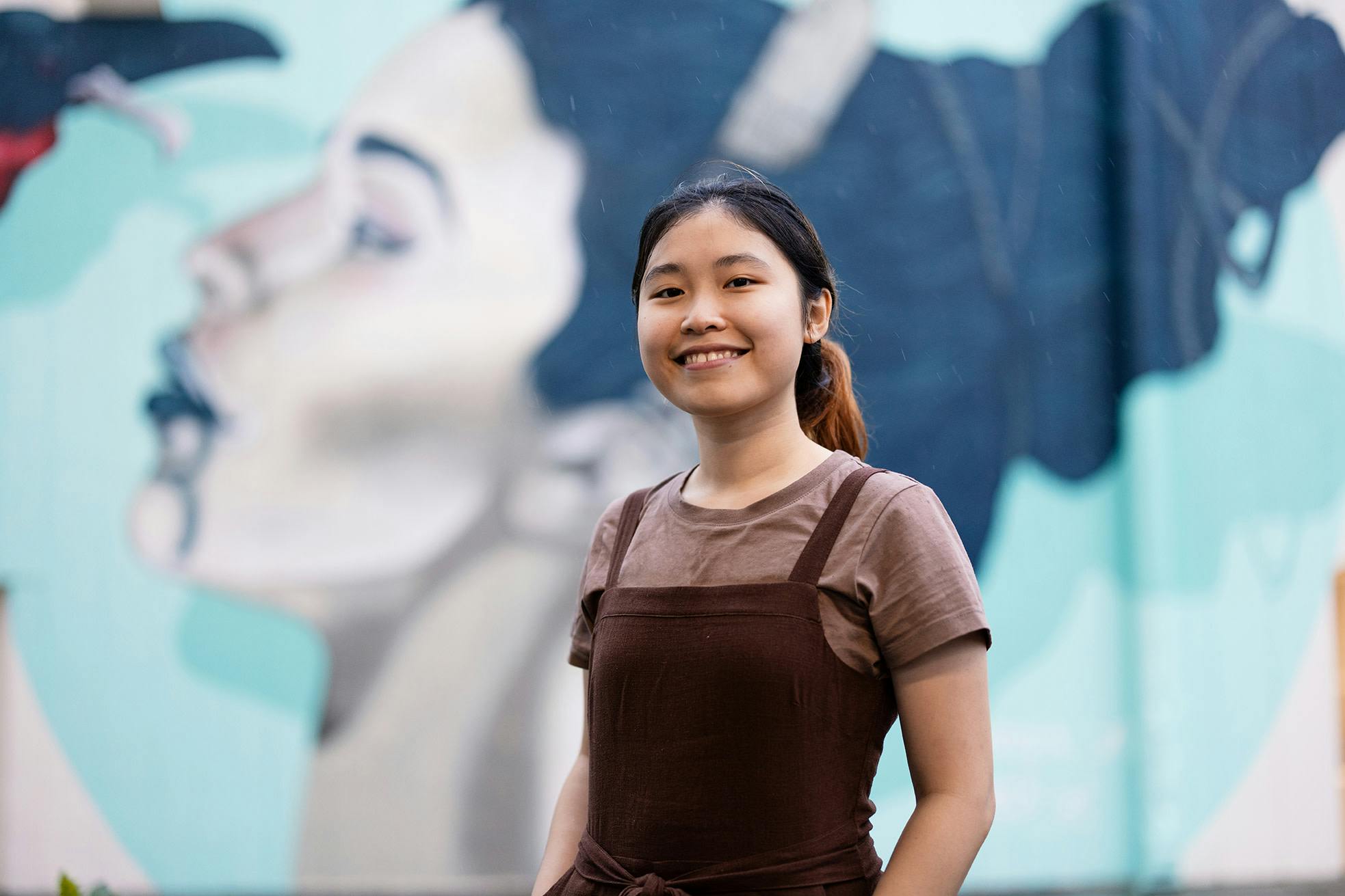 Ginny, a student from Thailand,  in front of a mural.