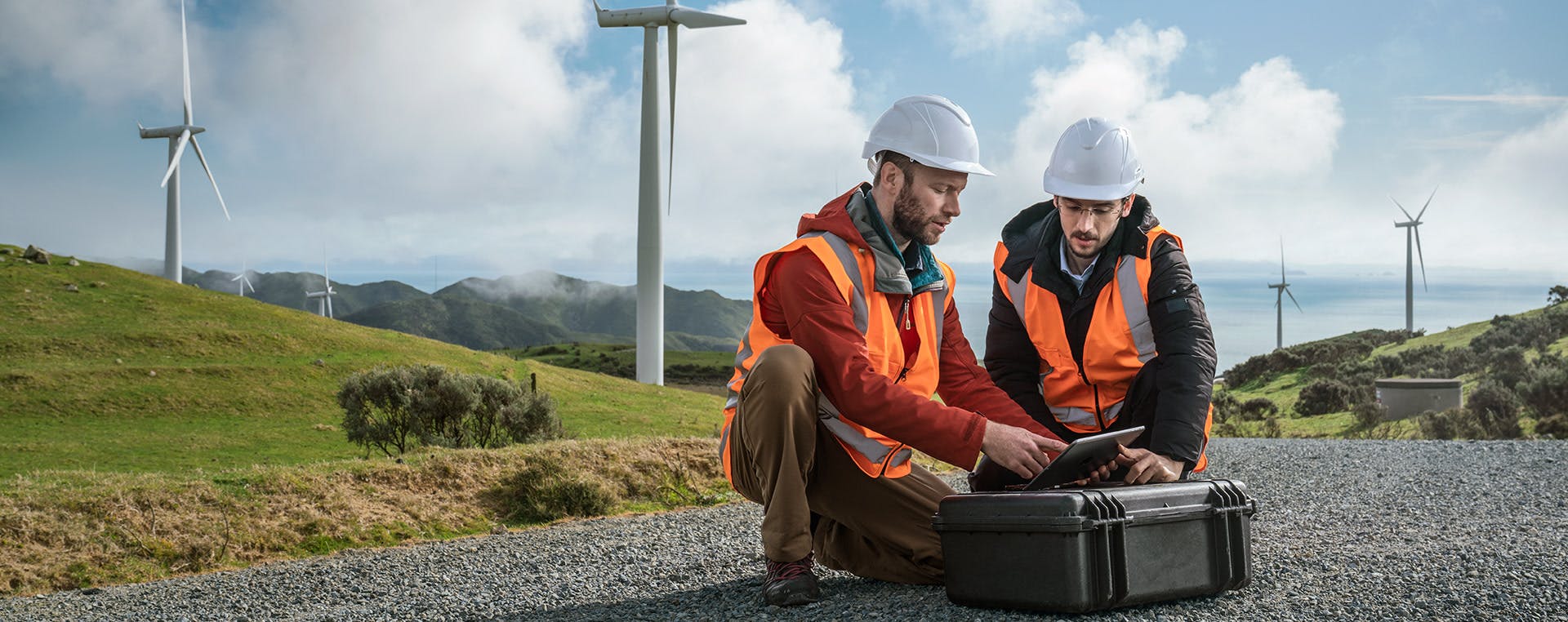 Engineering students work on a tablet, on site at a wind farm.