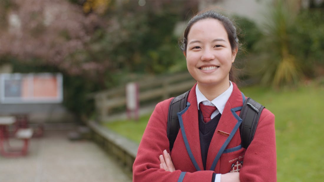 A proud international secondary school student smiles for the camera while posing outside her school