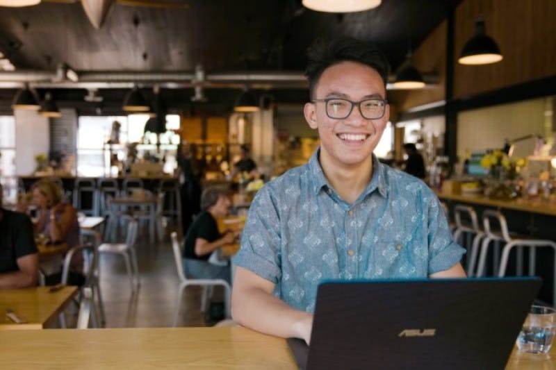 A smiling international student looks up from doing coursework in a café while on their laptop