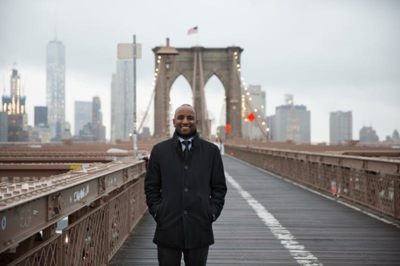 A smiling international student stands on the Brooklyn Bridge in New York City while looking at the camera