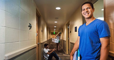 An international student who is a resident in a university hall smiles to the camera while other students are in the hallway