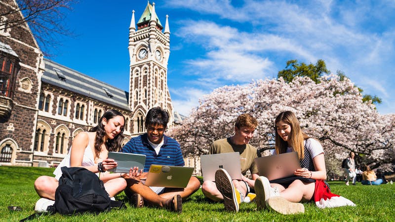 Students with laptops relaxing on the lawn of University of Otago campus