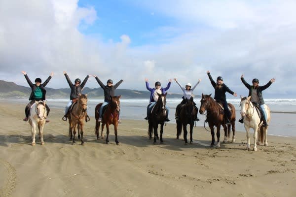 Seven horseback riders on a New Zealand beach pose for a photo with their horses